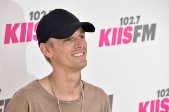 Aaron Carter smiling at an event, wearing a black cap and a casual shirt.