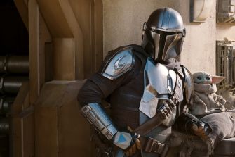 The Mandalorian in armor stands next to Grogu, a small creature, both set against a sci-fi backdrop.