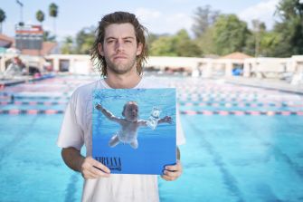 A man holding a reimagined cover of Nirvana's album "Nevermind" near a swimming pool.