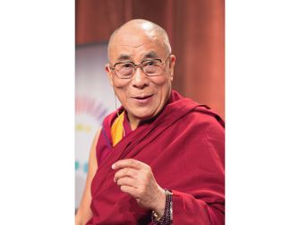 The Dalai Lama smiling and gesturing while wearing traditional garb.
