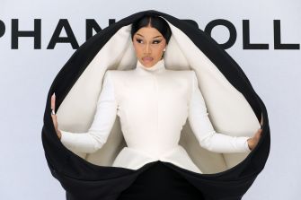 Cardi B in a striking black and white fashion ensemble, striking a pose with a dramatic backdrop.