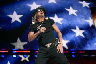 Kid Rock performing on stage in front of an American flag backdrop.