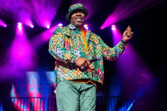 Busta Rhymes performing on stage during a live event with colorful lighting and attire.