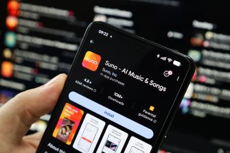 A hand holding a smartphone displaying the Suno AI music app on the screen, with a blurred background of social media posts.