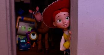 A scene from Toy Story 5 featuring Jessie, the cowgirl toy, peeking around a doorway with a joyful expression, surrounded by other toys.