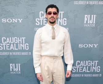 Bad Bunny attending the premiere of "Caught Stealing" in a cream-colored outfit and sunglasses.