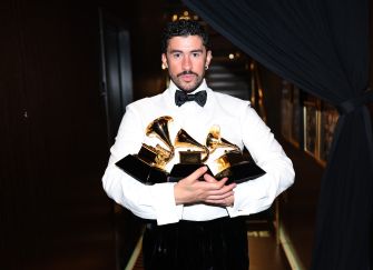 Bad Bunny holding multiple Grammy Awards while dressed in formal attire.