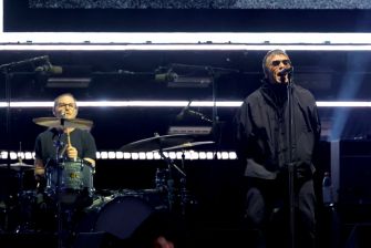 Oasis performing during their 2025 reunion tour, featuring the lead vocalist and drummer on stage.