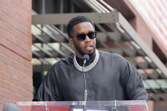 Sean Combs speaking at an event, wearing sunglasses and a black outfit.
