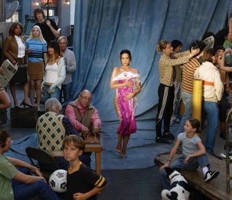A vibrant scene depicting a group of diverse individuals interacting, with one person in the foreground wearing a striking pink dress, set against a blue backdrop.