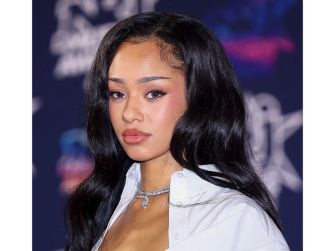 Image of a woman with long black hair wearing a white shirt, posing at a public event.