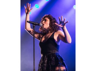 A performer on stage singing into a microphone with expressive hand gestures and dramatic lighting.
