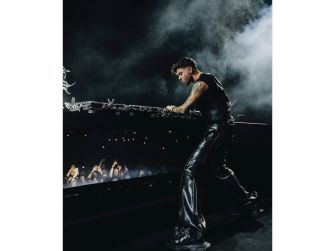 Anyma performing on stage with a crowd in the background during a music festival.