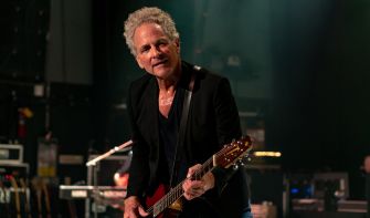 Lindsey Buckingham performing on stage with a guitar.