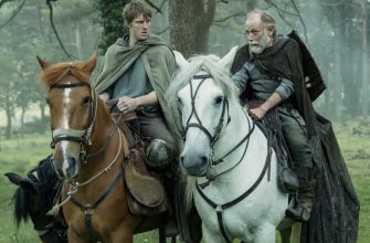 A young squire and an older man ride horses through a forest, dressed in medieval attire.