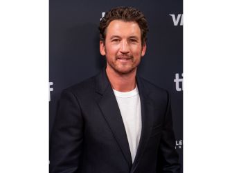 A man in a formal outfit poses for a photo at an event, with a dark background featuring the text "TIFF."