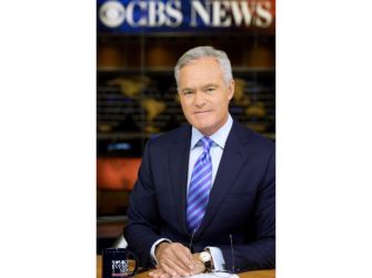 Scott Pelley seated at a CBS News desk, wearing a suit and tie, with a backdrop featuring the CBS News logo.