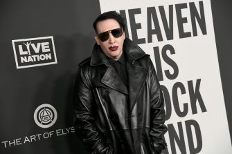 Marilyn Manson posing at a red carpet event, wearing a black leather coat and sunglasses.