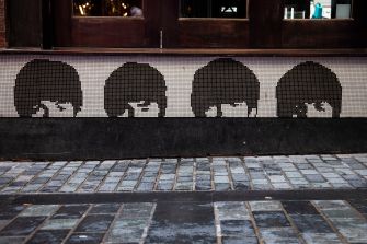 Mosaic artwork depicting stylized faces of four band members, displayed on a wall with a tiled surface.