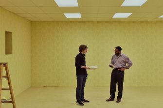 A director and an actor discuss a scene in a yellow-tinted room during the production of the film "Backrooms."