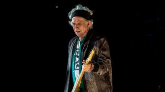 Keith Richards performing on stage with a guitar and smiling.