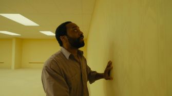 A man touching a yellow wall in an empty, surreal environment.