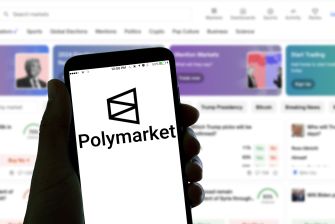 A person holding a smartphone displaying the Polymarket logo, with various betting options visible on the screen.
