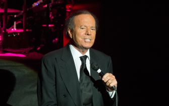 Julio Iglesias performing on stage, holding a microphone and wearing a suit.