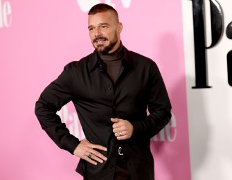 Ricky Martin posing at a red carpet event, wearing a black outfit and looking confident.