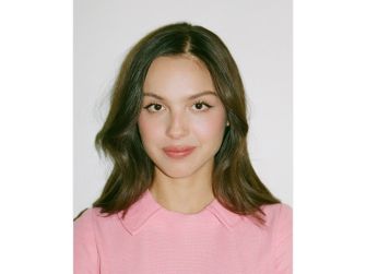 Portrait of Olivia Rodrigo wearing a pink dress, showcasing her hairstyle and makeup in a neutral setting.