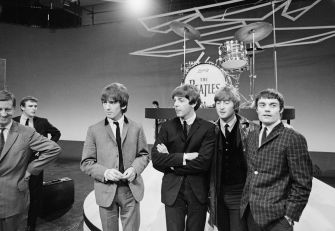 The Beatles on stage during their debut appearance, surrounded by production staff.