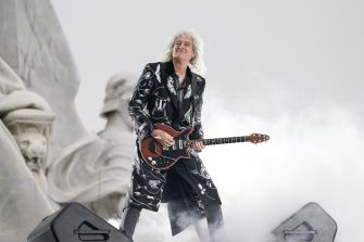 Brian May performing on stage with his guitar, wearing a distinctively patterned outfit.