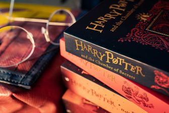 A close-up of stacked Harry Potter books, with a pair of round glasses resting nearby.