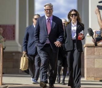 Alec Baldwin walking outside a courthouse with a woman, surrounded by others, amidst ongoing legal proceedings related to the 'Rust' shooting.