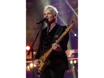 Sting performing on stage with a microphone and bass guitar, conveying his message about work and responsibility.