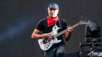 Tom Morello performing on stage with his guitar, wearing a cap and a red bandana.