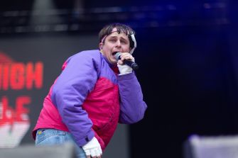 Oliver Tree performing on stage with a microphone, wearing a colorful outfit.