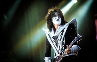 A guitarist in a striking costume with face paint performs on stage.