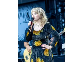 Singer-songwriter Violet Grohl performing live on stage with a microphone, wearing a floral dress.