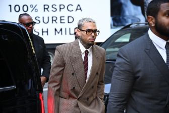 Chris Brown arriving at a court appearance, dressed in a formal suit and surrounded by security.