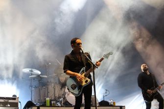 Placebo performing live on stage with dramatic lighting in the background.
