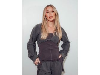 Hilary Duff poses in a stylish outfit, looking directly at the camera against a plain background.