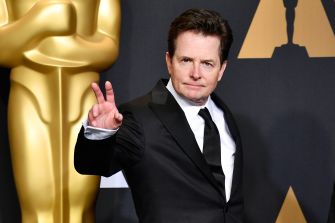 Michael J. Fox giving a peace sign on the red carpet at an awards event.
