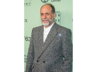 A man in a stylish, patterned suit poses for the camera against a light green backdrop with event branding.