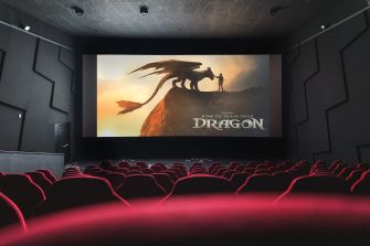 A movie theater interior featuring a large screen displaying the title "How to Train Your Dragon" with a dragon silhouette.