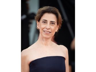 Fernanda Torres at a red carpet event, wearing a strapless navy gown and smiling at the camera.
