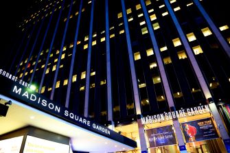 The exterior of Madison Square Garden, illuminated at night, featuring signage for the venue.