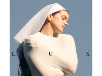 A close-up image of Rosalía featuring her in a white outfit and headscarf, positioned against a blue sky, with the album title "LUX" displayed to the sides.