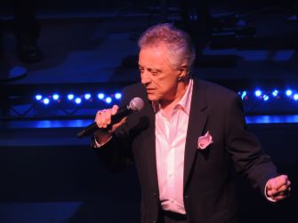 Frankie Valli performing on stage, holding a microphone.