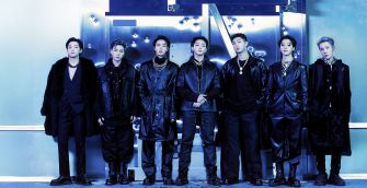 BTS posing together in stylish black outfits against a blue backdrop.